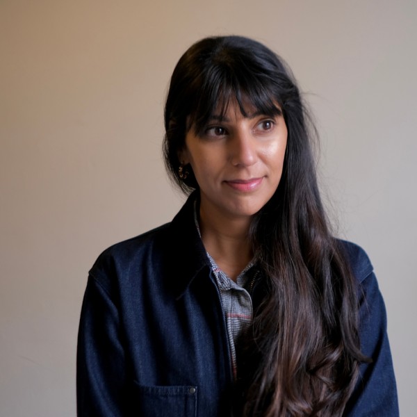 A photograph of Alycia Pirmohamed, a woman with brown skin and dark brown hair, wearing a denim jacket